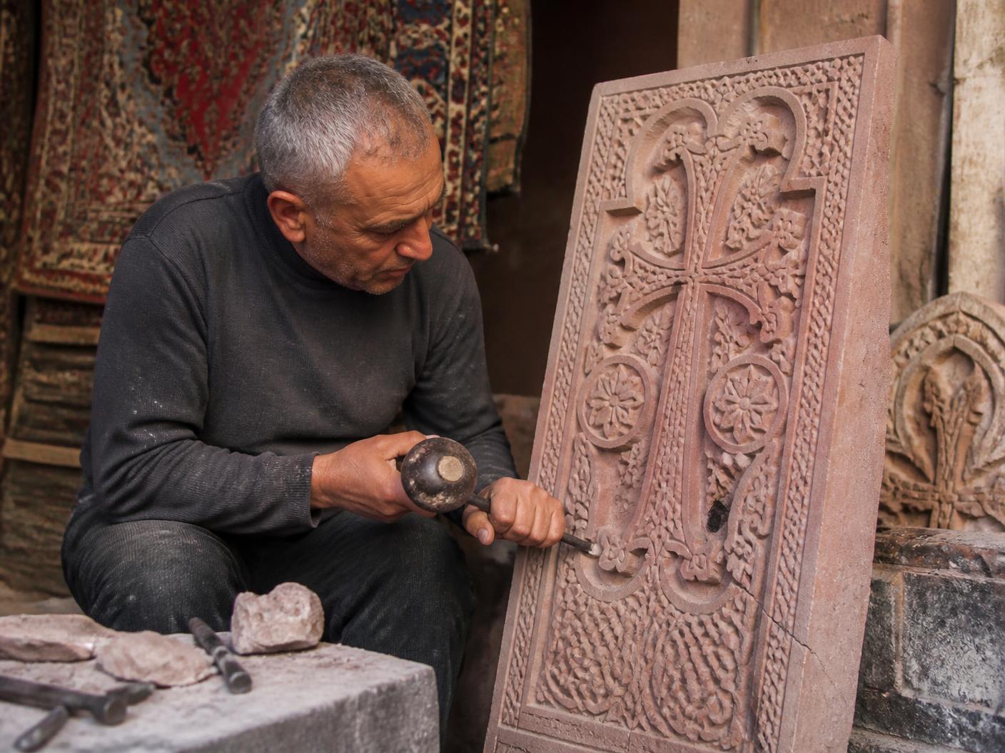 Armenian stone carver creating an intricate khachkar