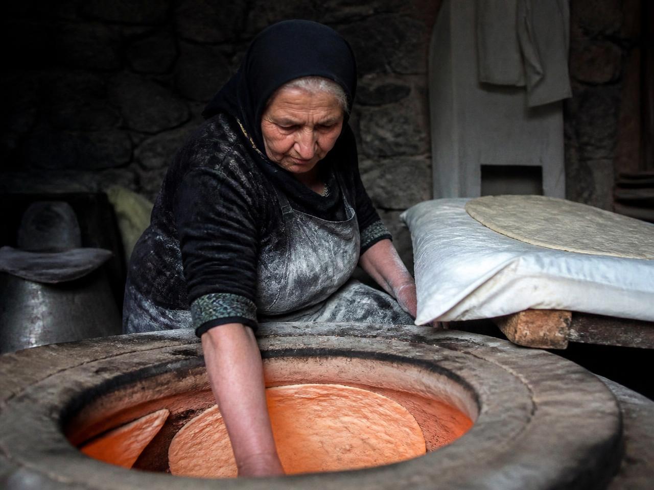 Sepia photograph of an Armenian woman kneading bread dough in a stone courtyard